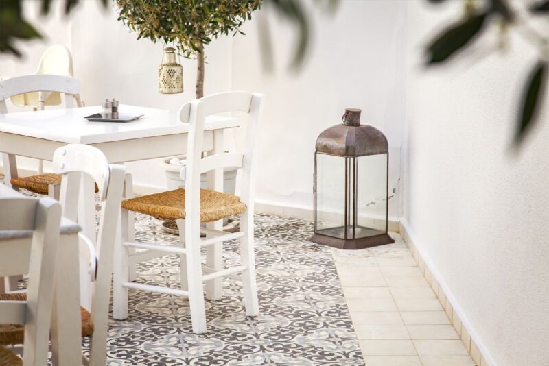 Small Mediterranean courtyard garden with simple white colours, with Moroccan style tiles, and a small table and chairs, with an olive tree in a white pot, and a glass old fashion styled lantern.