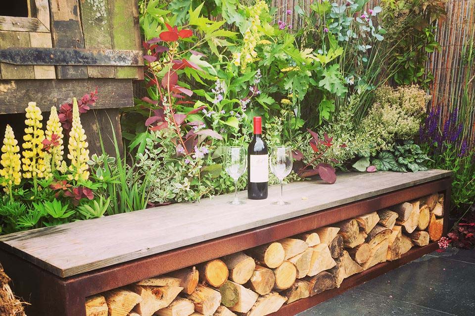 bench with wood storgae underneath with wine and glasses in a cozy garden