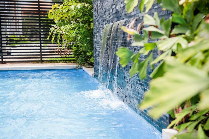 Mediterranean lifestyle with a beautifully blue splash pool with a water fall from a feature wall with a lovely colour of blue in teh pool and a small privacy screen to hide the swimming pool
