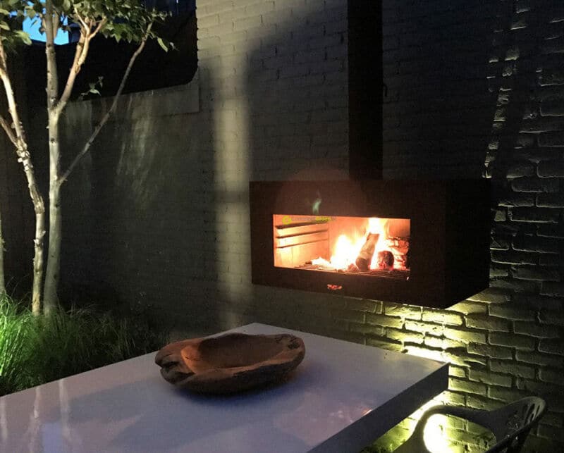 Outside wood burning black metal fireplace and a modern garden table at night with flames