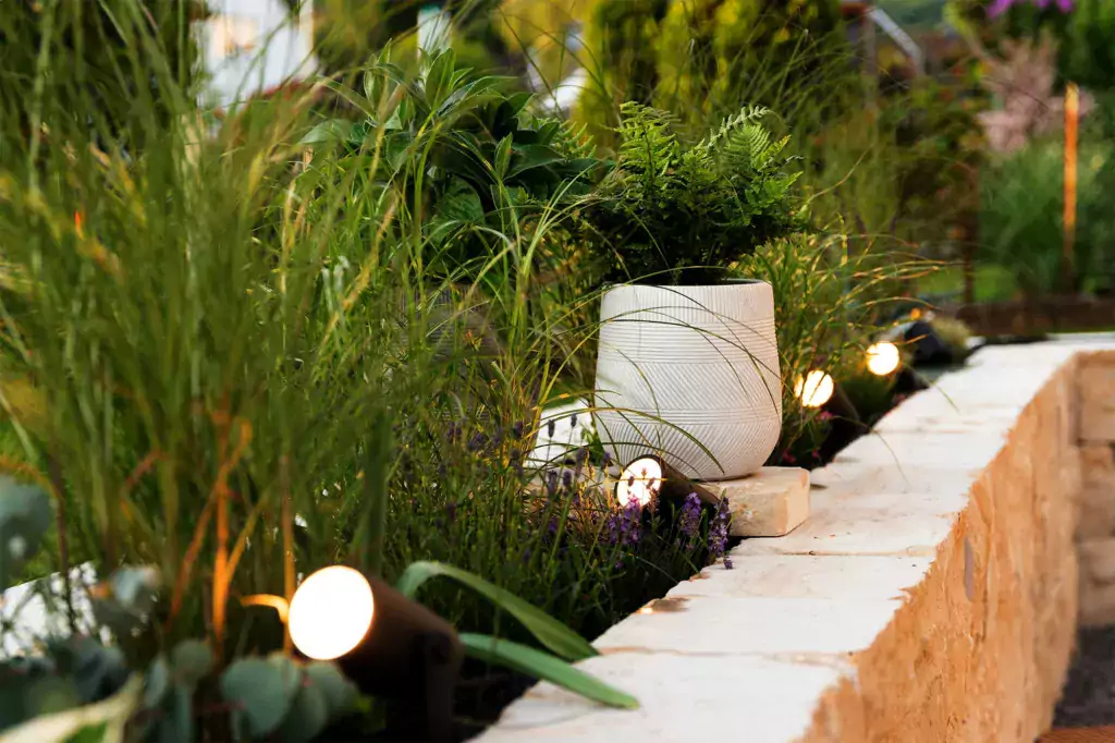 Garden lighting with spot lights in a raised bed with rich planting and a fern plant in a pot