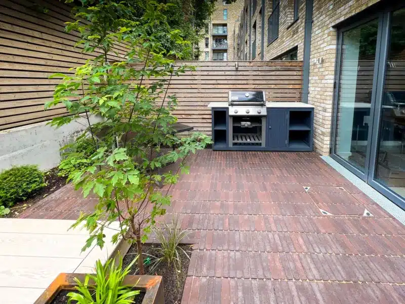 courtyard city garden with beautiful red clay pavers, with a venetian fencing around the permitter of the garden and handmade and bespoke outside kitchen which is ideal for this courtyard. The garden was designed and built by Luxury Garden design in Wimbledon. 