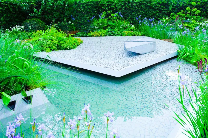 Ultra modern and Contemporary patio and terrace that is hanging over a luxury swimming pool and surrounded by lush green planting and rich blue pool colours. 