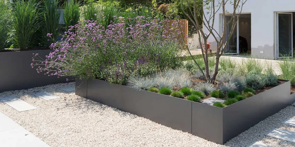 Mediterranean styled container garden with raised beds in grey aluminium with a gravel pathway and lots of green plants