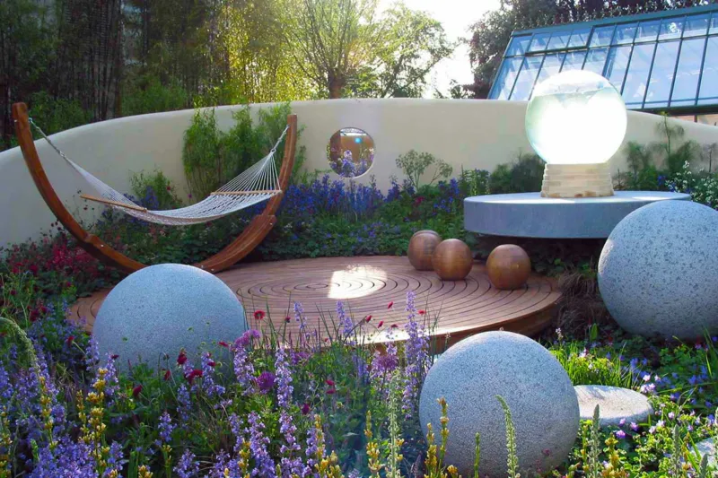 Modern Garden features with stone spheres and rendered wall with planting around a small wooden decking area and modern furniture in this garden