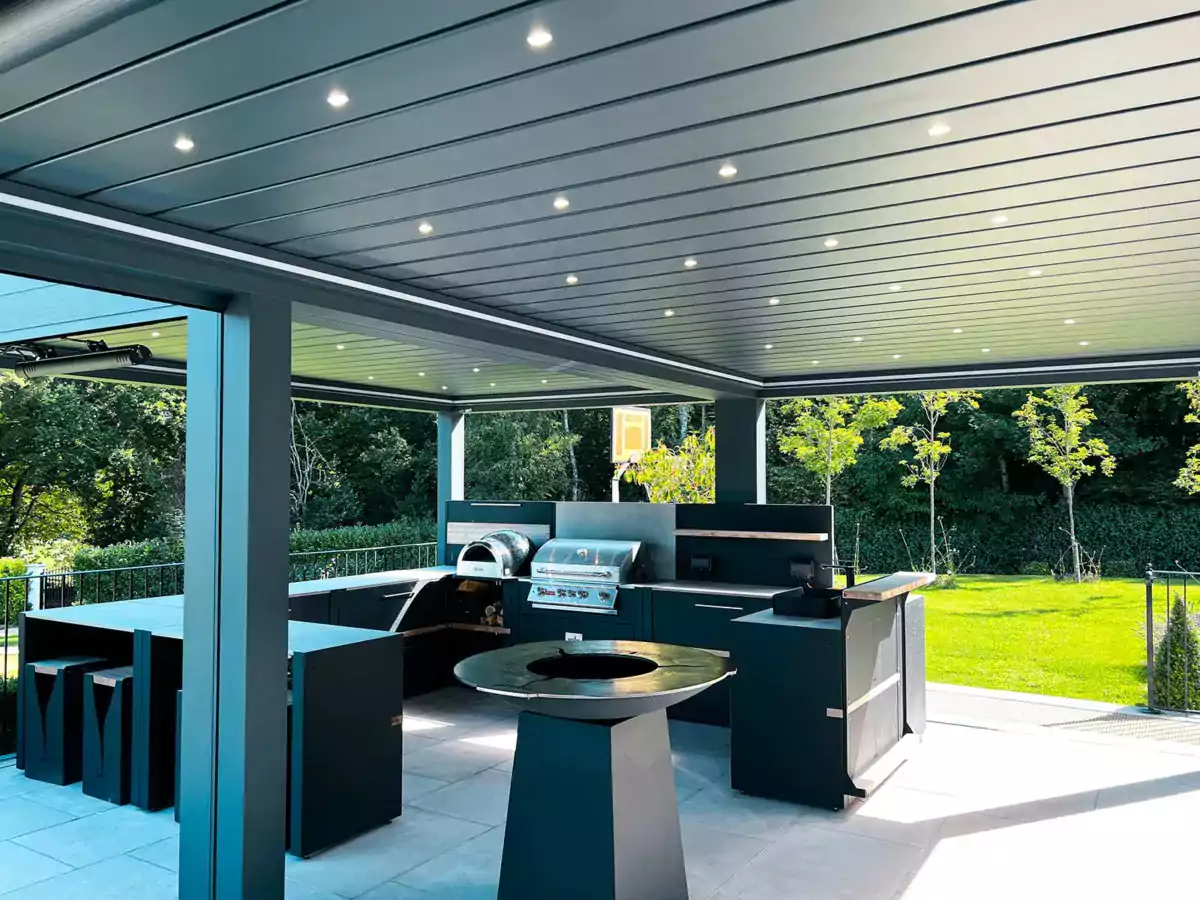 Stunning entertaining garden with an outside kitchen, wood fired anvil, gas BBQ, work tops, bar and sink all under a luxury pergola with lights that was designed and constructed by Luxury Garden Design.