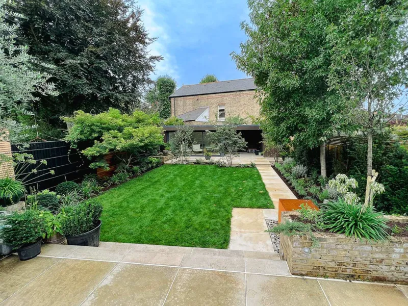 Medium-sized garden with a lawn area raised terrace near the house, and at the end, a garden office with a small terrace which you access by a path, which runs along the side of the lawn. The paving is smooth harvest sandstone, which is a sandy colour.