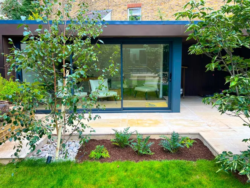 Modern garden office and building with a lovely smooth sandstone terrace that is screened by small trees and low planting