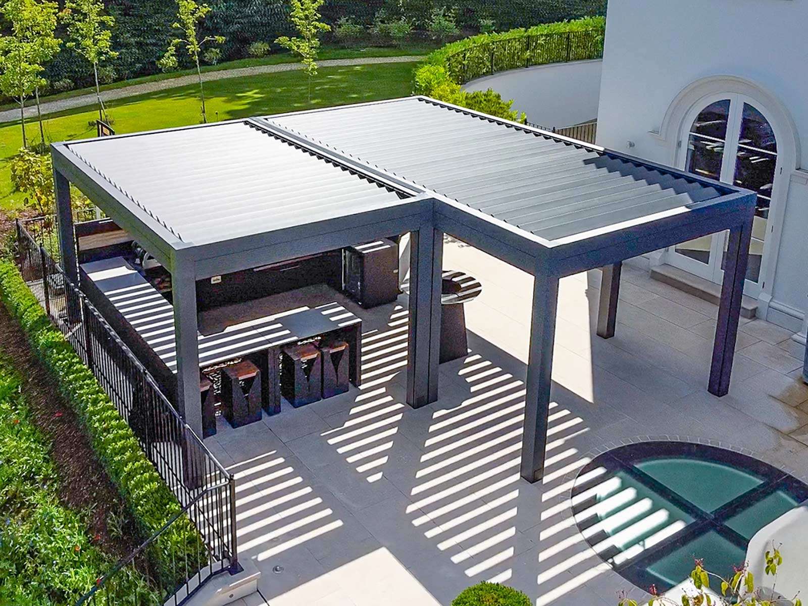 Luxury tailored garden design with fully automated aluminum pergola and wonderful outside kitchen on an elevated limestone terrace.