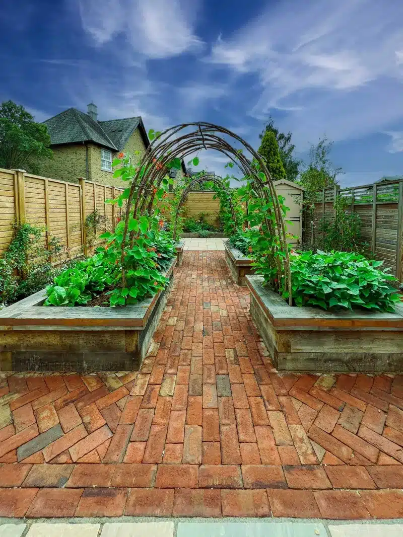 oak raised beds in a vegetable garden with hazel arches and red clay brick pavers