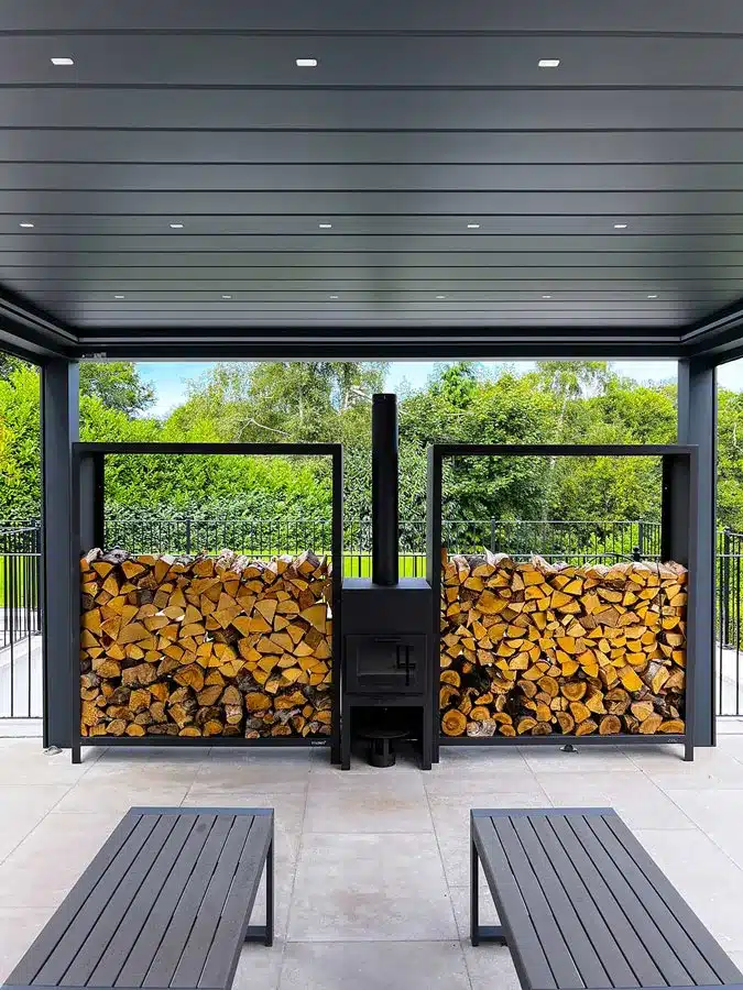 An aluminium garden pergola in a contemporary garden a large outside wood fireplace and log storage each side to create a feature wall.